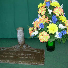 Colorful floral arrangement beside a memorial plaque and vase