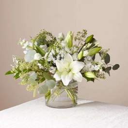 White lilies and delicate white blooms arranged in a clear glass cylinder vase