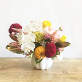 Mixed floral arrangement in a white pumpkin vase with white orchids and yellow blooms