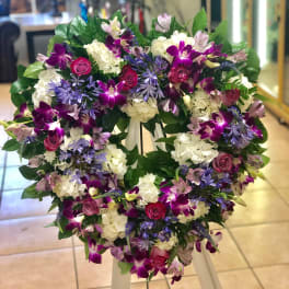 Heart-shaped standing wreath with purple orchids, pink roses, and white hydrangeas on a white easel