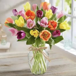 Mixed-color tulip bouquet arranged in a clear glass vase tied with twine.