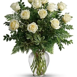 White roses with abundant greenery arranged in a clear glass vase