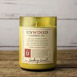 Yellow scented candle in a green glass jar with a printed label on a wooden surface