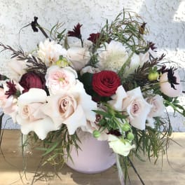 Mixed bouquet of pale roses and red blooms in a lavender vase