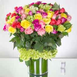 Large multicolored rose arrangement with green hydrangea in a clear glass vase