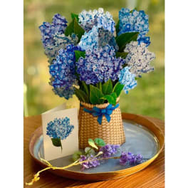 Blue and purple hydrangea-style silk flowers in a basket with matching card on a tray