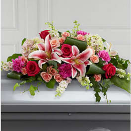 Pink lilies, red and peach roses, and mixed blooms arranged as a casket spray on a gray casket