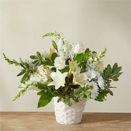 White lilies, roses, and other white flowers arranged in a white woven basket