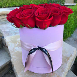 Red roses arranged in a lavender hat box with a ribbon bow