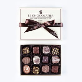 Box of assorted gourmet chocolates with lid and ribbon beside it