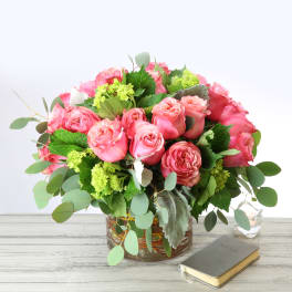 Low arrangement of pink roses and green accents in a glass vase with eucalyptus