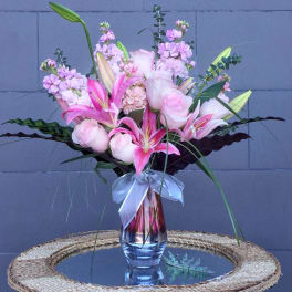 Pink lilies and roses arranged in a glass vase with a ribbon