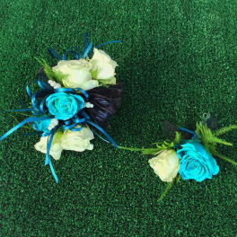 Two small rose corsages with blue ribbon accents on green turf