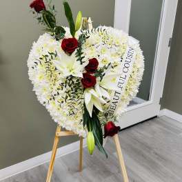 Heart-shaped white floral wreath with red roses and lilies on an easel