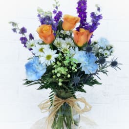 Bouquet of orange roses, blue carnations, and purple flowers in a glass vase