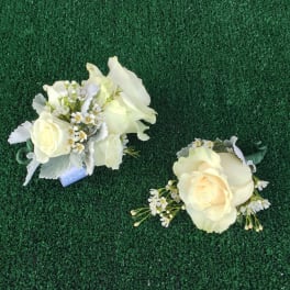 Two ivory rose corsages with small white flowers on green turf