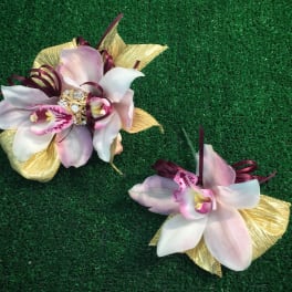 Two orchid corsages with gold ribbon accents on green turf