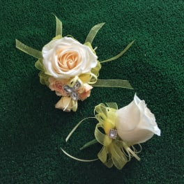 Two white rose corsages with pale green ribbon accents on a dark green surface