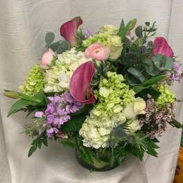 Mixed arrangement of pink calla lilies, roses, and hydrangeas in a clear glass vase
