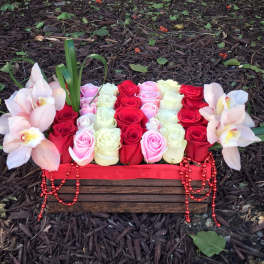 Rectangular floral arrangement with red, pink, and white roses and pale orchids in a wooden box