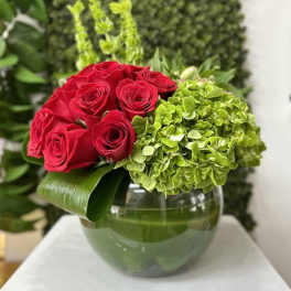 Low arrangement of red roses and green hydrangeas in a round glass vase