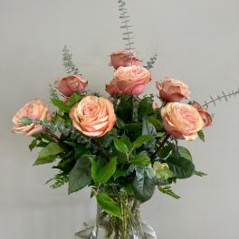 Peach roses arranged in a clear glass vase with greenery.