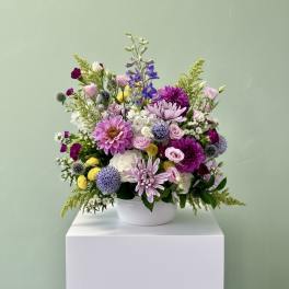 Mixed bouquet of pink, purple, white, and yellow flowers in a white bowl vase