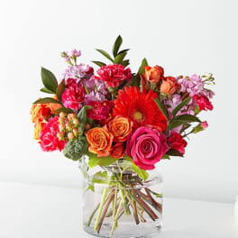 Bright mixed bouquet of roses, gerbera daisies, and carnations in a clear glass vase