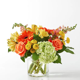 Mixed bouquet of orange, yellow, and green flowers in a clear glass vase