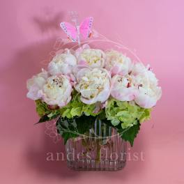 Pink and white peonies in a clear glass vase with a butterfly pick