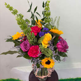 Mixed bouquet of roses, carnations, and sunflowers in a glass vase