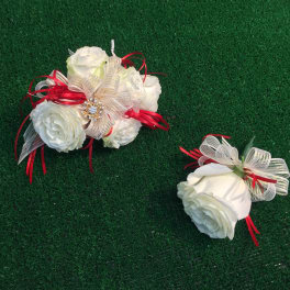 Two white rose corsages with red and gold ribbon accents