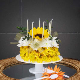 Yellow and white flower cake with candles on a white stand