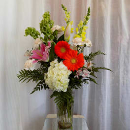 Tall mixed bouquet in a glass vase with pink lilies, orange gerberas, and white hydrangea