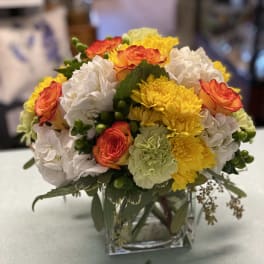 Mixed bouquet of orange roses, white hydrangeas, and yellow chrysanthemums in a glass vase