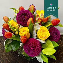 Bouquet of yellow roses, orange tulips, and purple dahlias in a glass vase