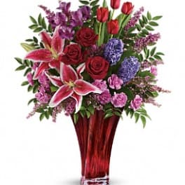 Mixed bouquet of red roses, pink lilies, and purple flowers in a red vase