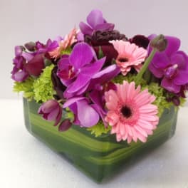 Pink gerbera daisies and purple orchids in a green glass vase