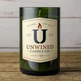Green glass jar candle with cream label reading Unwined Candle Co. on a wooden surface