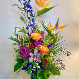 Tropical bouquet with orange bird-of-paradise and mixed blooms in a glass vase