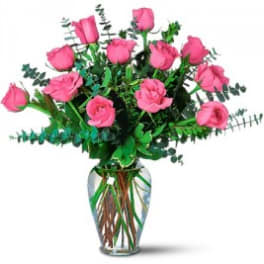 Pink roses arranged in a clear glass vase with greenery