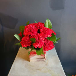 Red carnation arrangement in a wooden box with a red ribbon