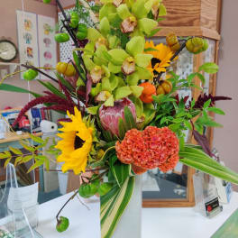Tall mixed floral arrangement in a white vase with green orchids and sunflowers