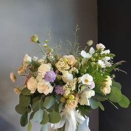 Loose bouquet of cream and white flowers in a glass vase with a white ribbon.