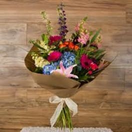 Mixed bouquet with blue hydrangeas, pink lilies, and bright flowers wrapped in brown paper