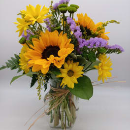 Bouquet of yellow sunflowers and purple flowers in a glass vase