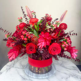 Red floral arrangement in a glass vase with a wide red ribbon