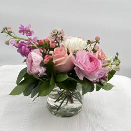 Low arrangement of soft pink and white roses and ranunculus in a clear glass vase.