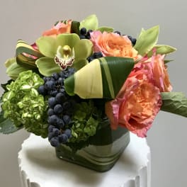Bouquet of orange roses, green orchids, and hydrangeas in a square vase