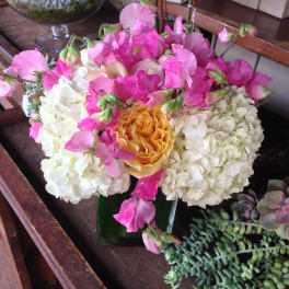 Pink sweet peas and white hydrangeas around a yellow rose in a glass vase